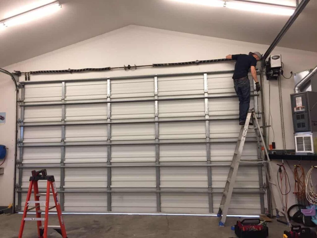Technician repairing a large garage door spring mechanism