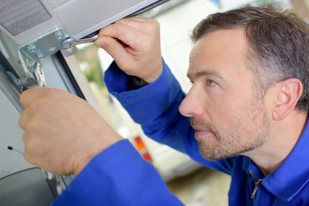 Man in blue overalls repairing a garage door mechanism